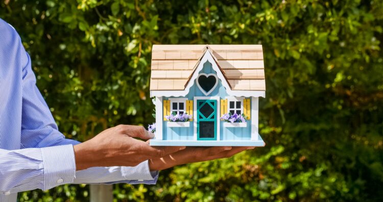 Professionista immobiliare che tiene una casa delle bambole, a simboleggiare quanto sia facile acquistare e vendere case con i-buyers